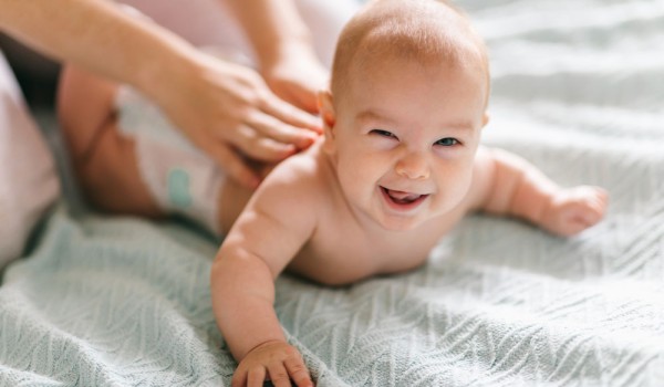 Baby erhält Rückenmassage und guckt verschmitzt