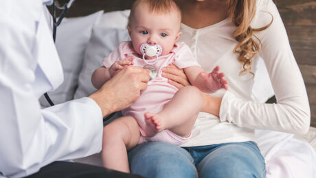 Arzt hört Baby ab, welches auf dem Schoß der Mutter sitzt