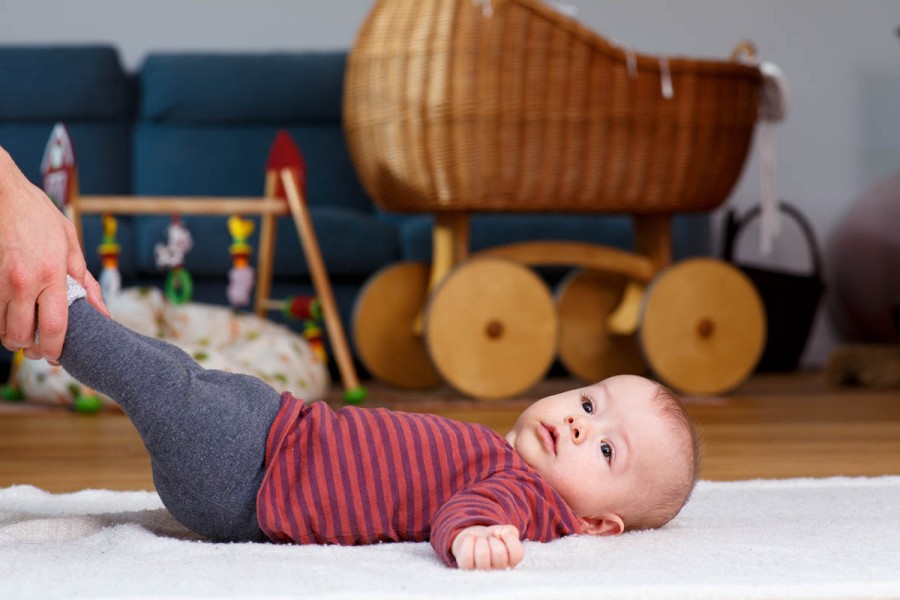 Baby liegt auf dem Rücken am Boden und die Hände eines Elternteils umfassen seine Füßchen
