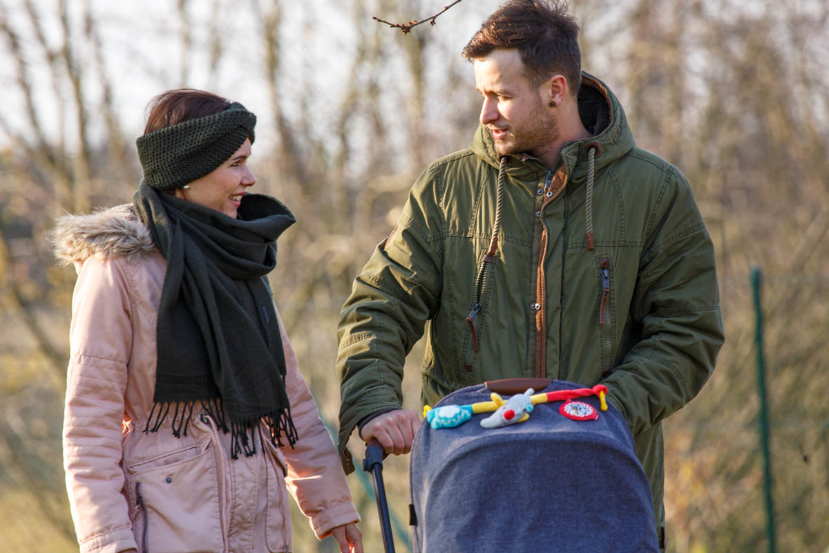 Paar spaziert mit Kinderwagen im Park.