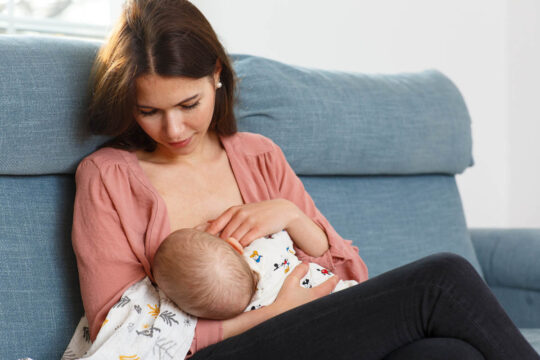 Mutter stillt ihr Baby auf einem Sofa.