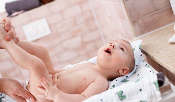 Ein Baby wird auf einem Wickeltisch gewickelt.  Seine Beine werden von Erwachsenenhänden gehalten.