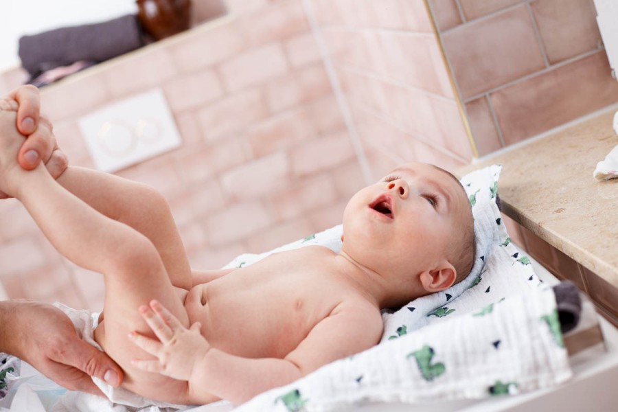Ein Baby wird auf einem Wickeltisch gewickelt.  Seine Beine werden von Erwachsenenhänden gehalten.