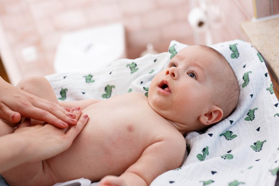 Babymassage: Hände massieren Babybauch auf gemusterter Decke.