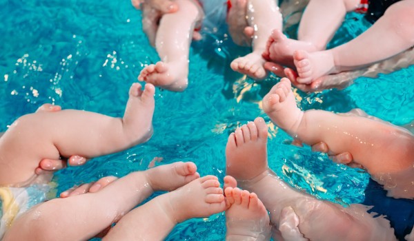 Babys im Schwimmkurs: Kleine Füße und Beine im türkisblauen Wasser.