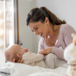 Mutter spielt mit ihrem dreimonatigen Baby im Schlafzimmer. Beide schauen sich freudig an.