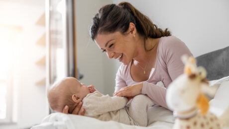 Mutter spielt mit ihrem dreimonatigen Baby im Schlafzimmer. Beide schauen sich freudig an.