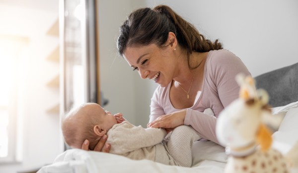 Mutter spielt mit ihrem dreimonatigen Baby im Schlafzimmer. Beide schauen sich freudig an.