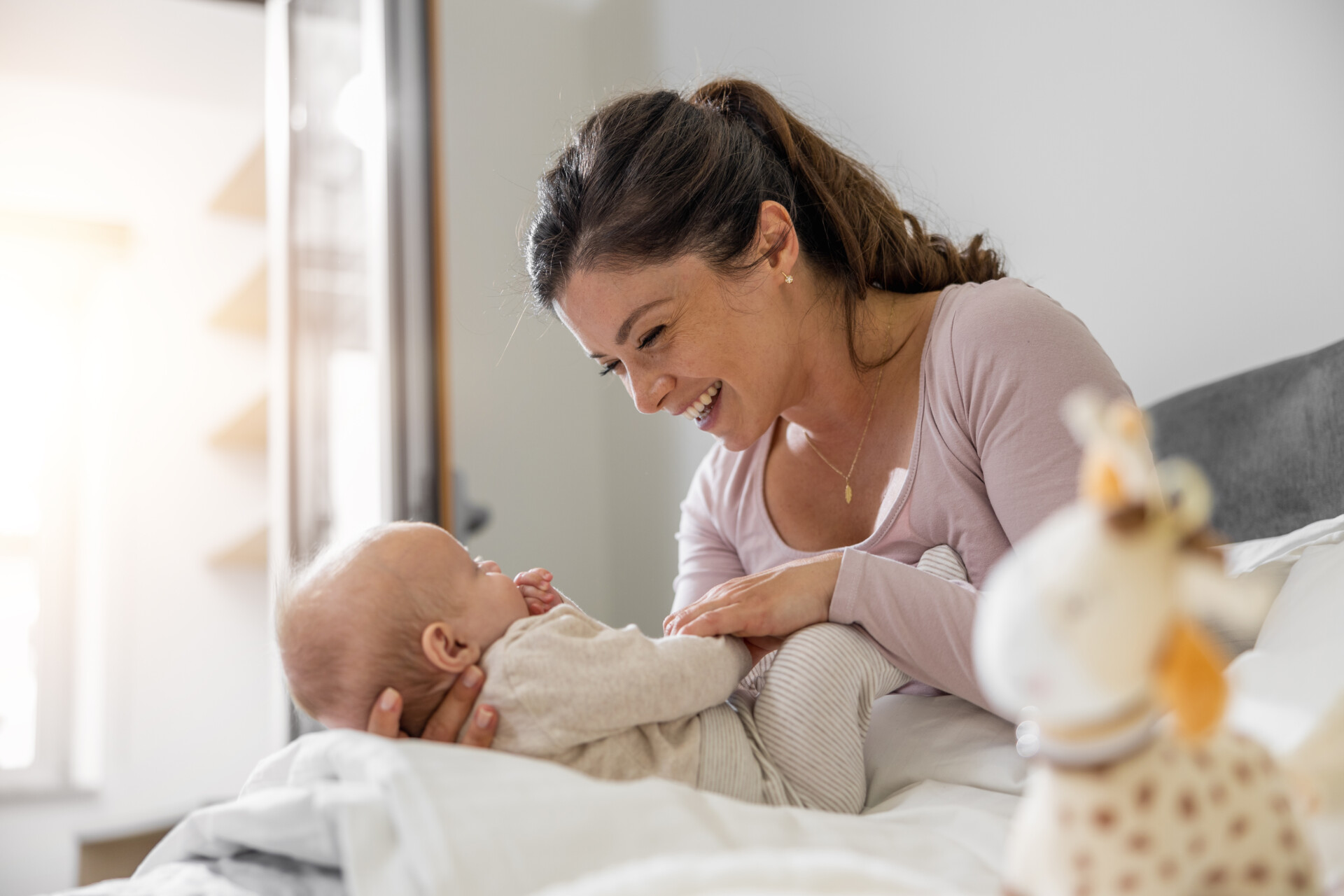 Mutter spielt mit ihrem dreimonatigen Baby im Schlafzimmer. Beide schauen sich freudig an.