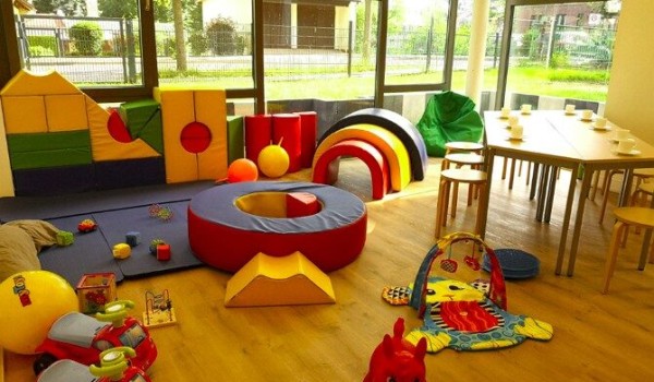 Bunt bespielter Spielraum mit Kletterelementen, Spielzeug und Tisch mit Stühlen.